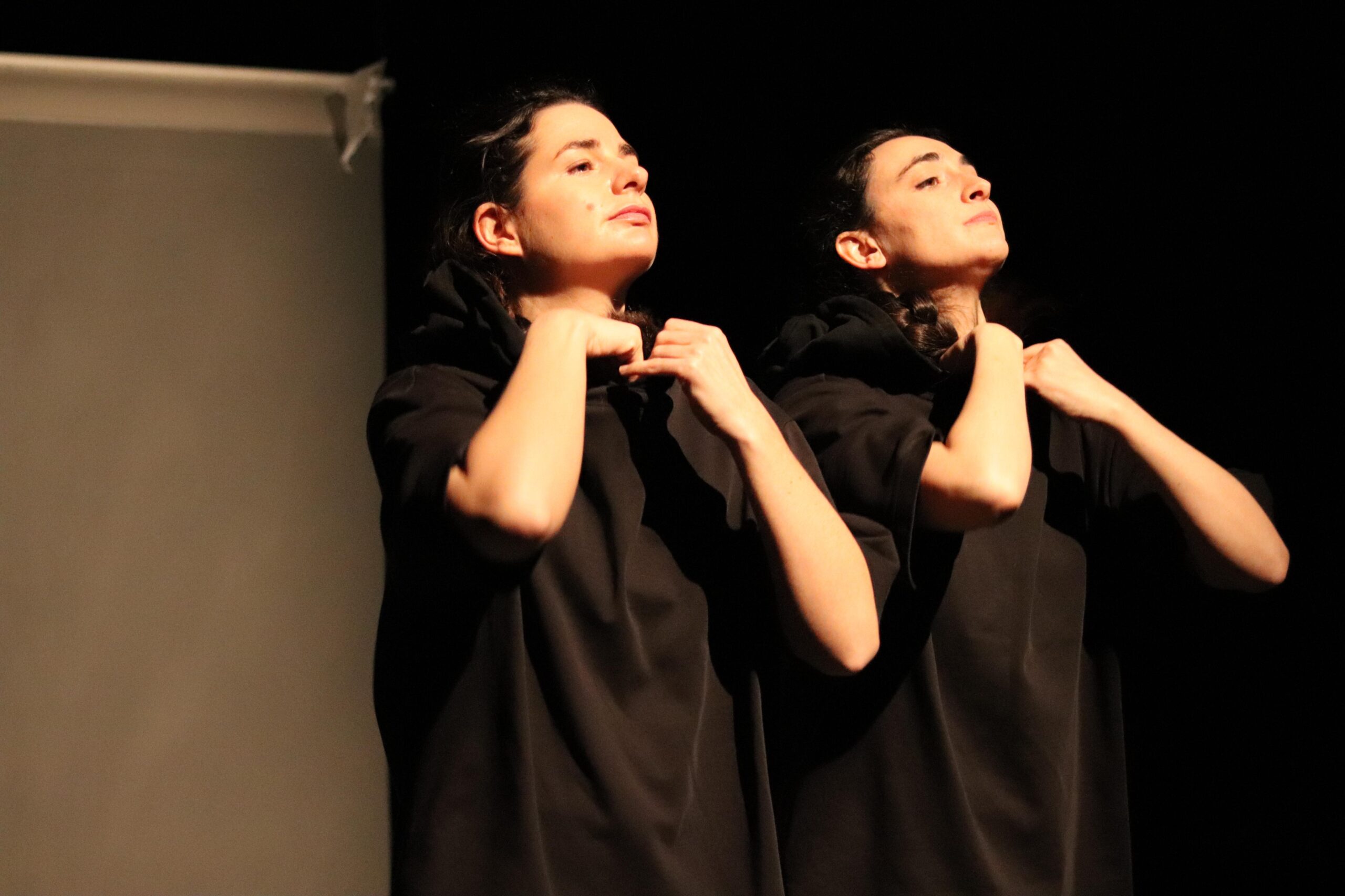 Deux comédiennes, tout en noir, se réajustent le col. Elles regardent toutes les deux en face d'elles, comme en face d'un miroir.