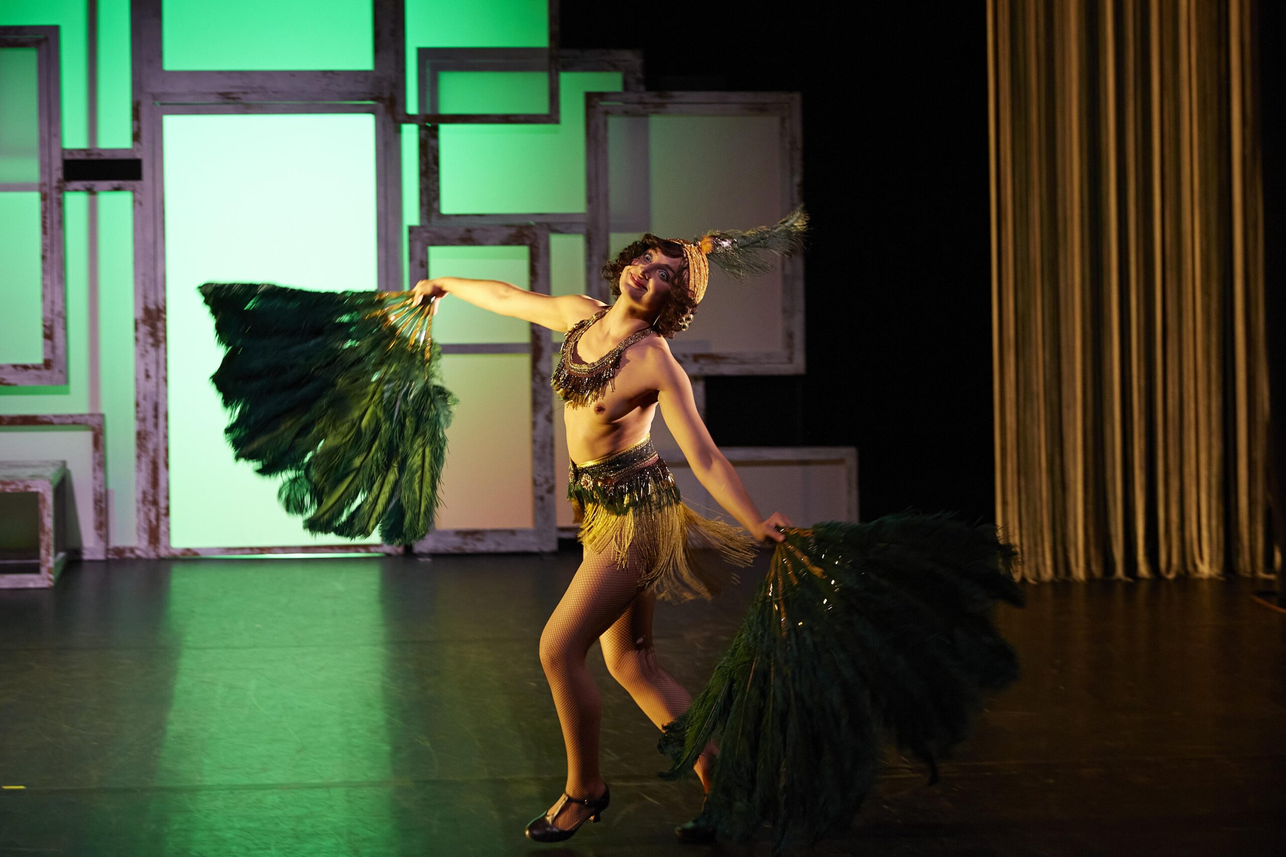 Une femme, presque nue, danse. Elle brandit de gigantesques éventails en plumes vertes. Elle porte des chaussures à talons, des bas résille, une petite jupette à franges, un collier de perles massif et un turban avec une plume.